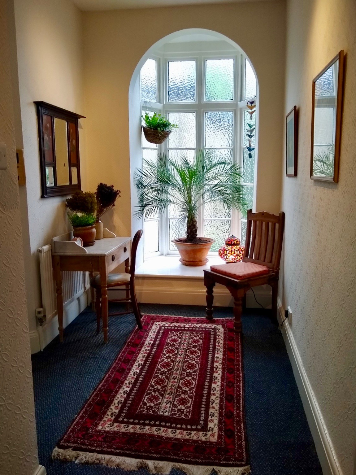 Arched window in the hallway with desk, chairs and a large plant