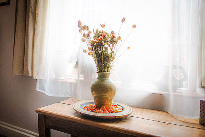 A metal vase and plate with a dried slower display infront a a bright window