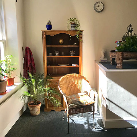 A sunny corner with wicker chair, bookshelf and plant at The Practice Rooms in Richmond, London