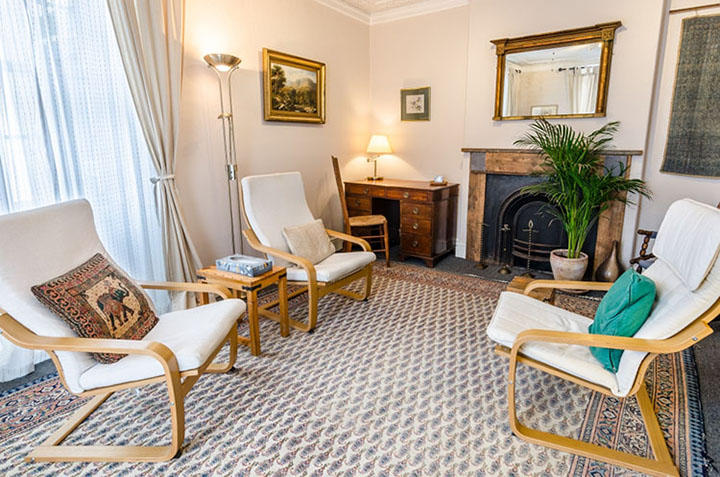 A large therapy room with 3 chairs, desk and a fireplace at The Practice Rooms in Westbury-on-Trym, Bristol